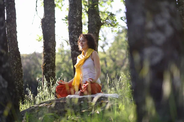 Gün batımında ağaçların arasında meditasyon yapan genç bir kadın..