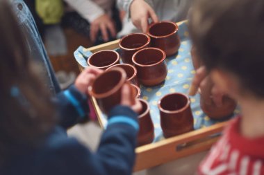 Children's hands picking up earthenware bowls with water in the Waldorf school cast. clipart