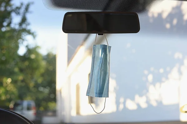 Surgical mask hanging from the mirror inside the car. Concept of new normality.