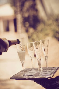 Garson sepya tonlarında açık hava düğününde köpüklü şampanya kadehleri servis ediyor..