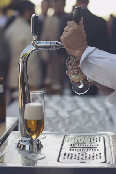 Waiter throwing beer on an open-air bar tap in vertical detail.