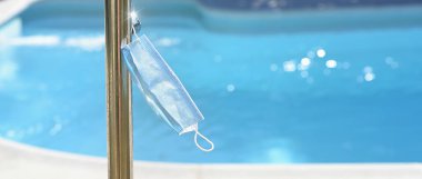 Yüzme havuzundaki duş musluğundan sarkan cerrahi maske. Tuvalet için toplum standartlarını kabul et..