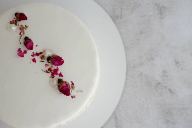 Süt ve böğürtlen dolgulu kurumuş gül tomurcuklarıyla süslenmiş pürüzsüz jöleli beyaz kremalı pasta, yakın çekim. Boşluğu kopyala