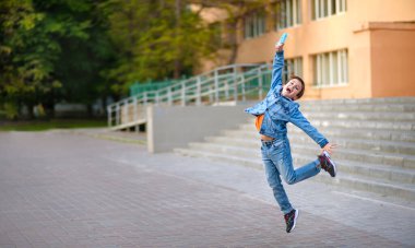 Okul bahçesinde zıplayan mutlu çocuk karantinanın sona ermesine seviniyor. Çocuk maskesini çıkardı ve elinde koruyucu maskeyle neşeyle atladı. Duygusal Çocuk, Salgının Sonu 2020