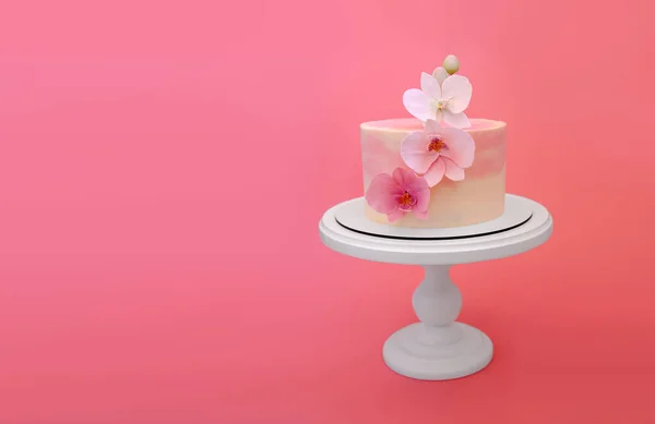 Pink marble cake stands on a round white stand on a pink background. Cake decorated with sugar flowers orchids. Beautiful dessert decorated with flowers.