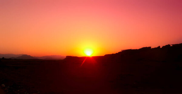 Dawn in the desert. The bright orange sun rises from behind the mountains. Nature background
