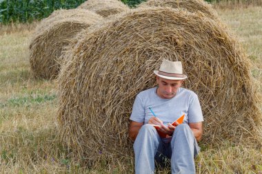 Çiftçi Hasır Bale 'e yaslanırken Not Defterine Yazıyor