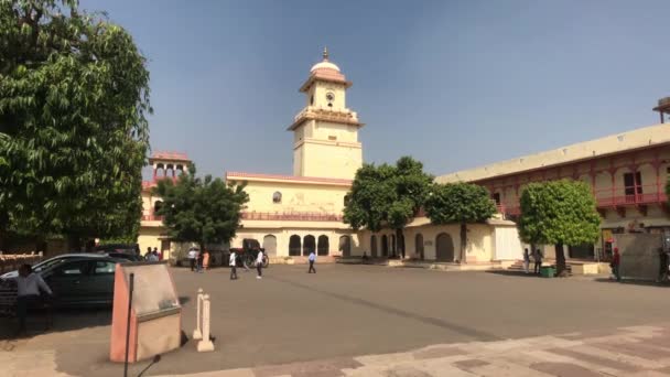 Jaipur, India - 04 de noviembre de 2019: Los turistas del Palacio de la Ciudad caminan alrededor de la plaza contra el telón de fondo de una torre del reloj — Vídeos de Stock