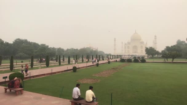 Agra, India, 10 de noviembre de 2019, Taj Mahal, los turistas se sientan en un banco cerca del césped — Vídeo de stock