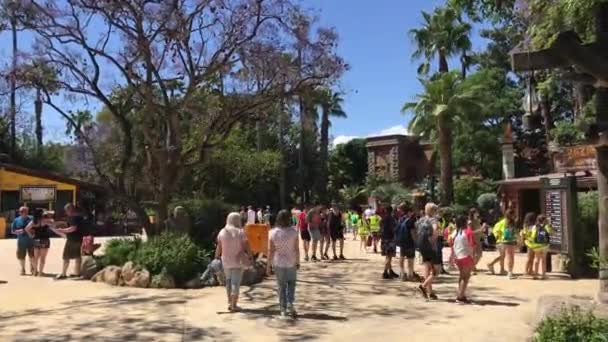 Salou, Spanje, 28 juni 2019: Een groep mensen die wandelen in een park met Pearl Street Mall op de achtergrond — Stockvideo