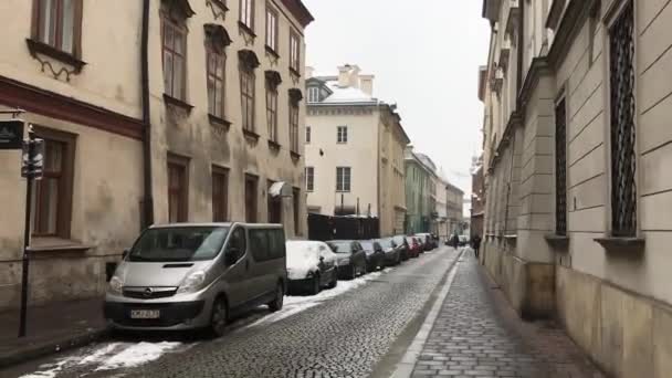 Krakkó, Lengyelország, egy keskeny városi utca, egy épület oldalán parkoló autókkal — Stock videók