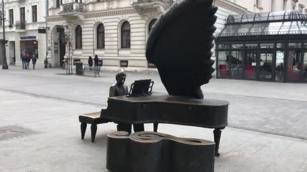 Lodz, Polônia, Uma estátua de uma pessoa sentada em um banco em frente a um edifício — Vídeo de Stock