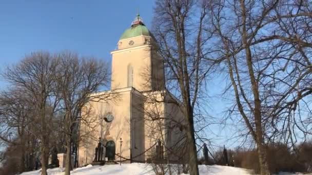 Helsinki, Finlandia, Wieża zegarowa pokryta śniegiem z kościołem parafialnym Bruton w tle — Wideo stockowe