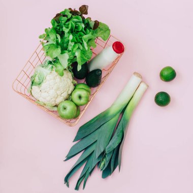 Yeşil meyve ve sebzeler üzerinde pastel pembe bir arka plan ile sepet