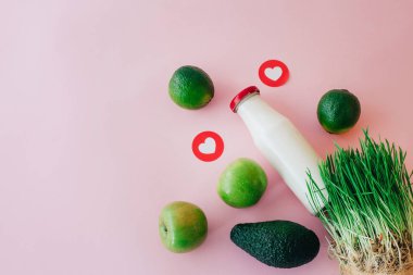Pastel pembe bir arka plan üzerinde elma, limon ve avokado şişe ve yeşil çim ile üstten görünüm