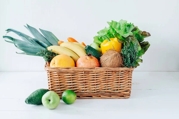 Wicker basket with fresh vegetables and fruits on white background