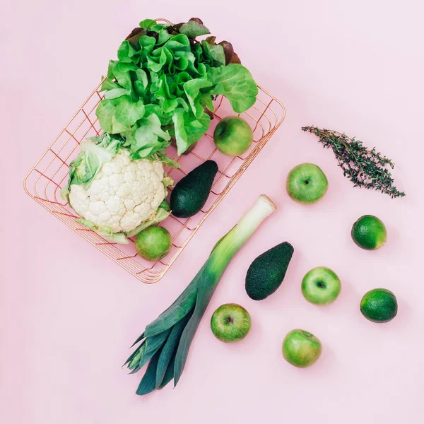 Basket with green fruits and vegetables on pastel pink background