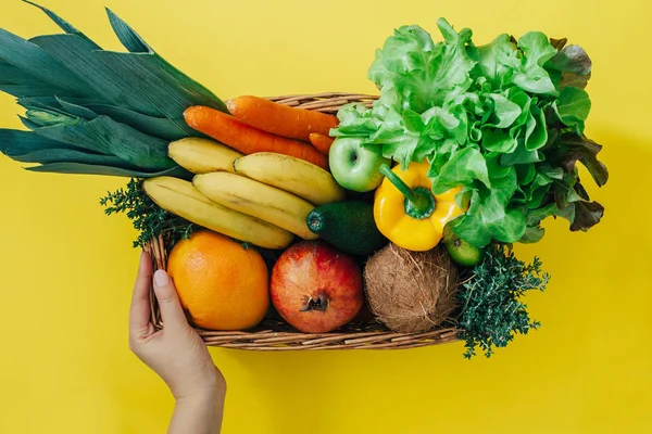 Wicker basket with fresh vegetables and fruits on yellow background
