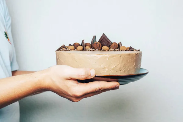 Chocolate cake in male hands on a blue plate. Sweet gift. Birthday. Valentine\'s Day. Chef. Homemade baking. Sponge cake with cream.