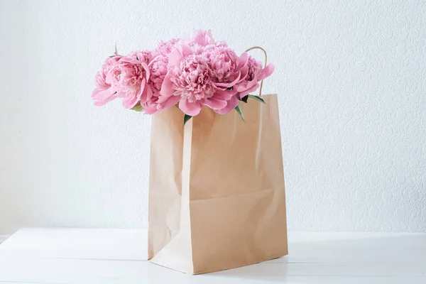 Pembe peonies beyaz bir tabloda bir kağıt torba