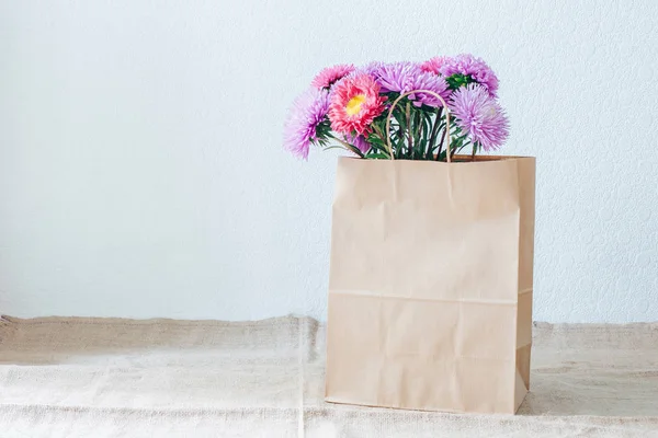 Bouquet of asters. Paper bag. Eco-packaging. Flower delivery. Green vase. Pink flowers. Autumn Bouquet.