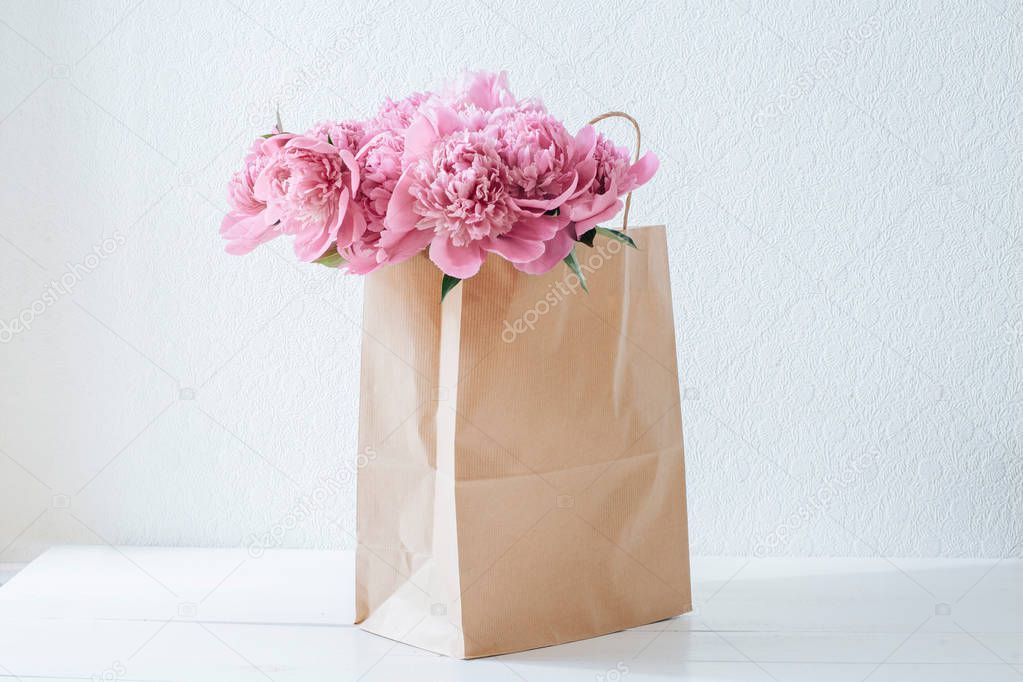 Pink peonies in a paper bag on a white table