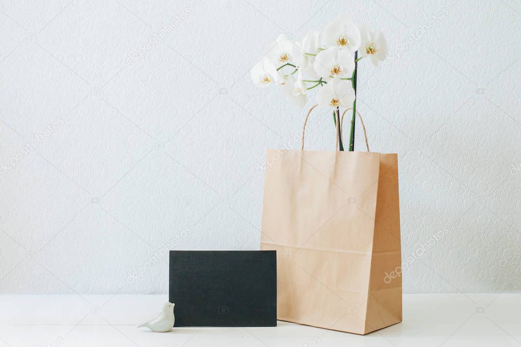 Orchids in a paper bag. White orchids. Paper bag. White table. White wallpapers. Flowers in a paper bag.