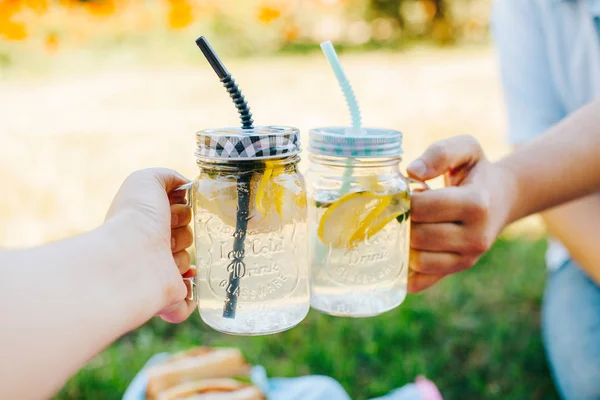 People toasting with two mason jar glasses of homemade lemonade on a rustic wooden background