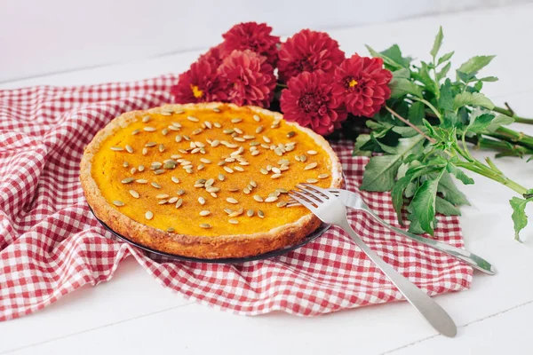 Sweet pumpkin pie on plate with forks, napkin and red flowers