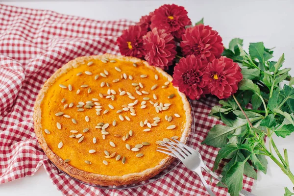 Sweet pumpkin pie on plate with forks, napkin and red flowers