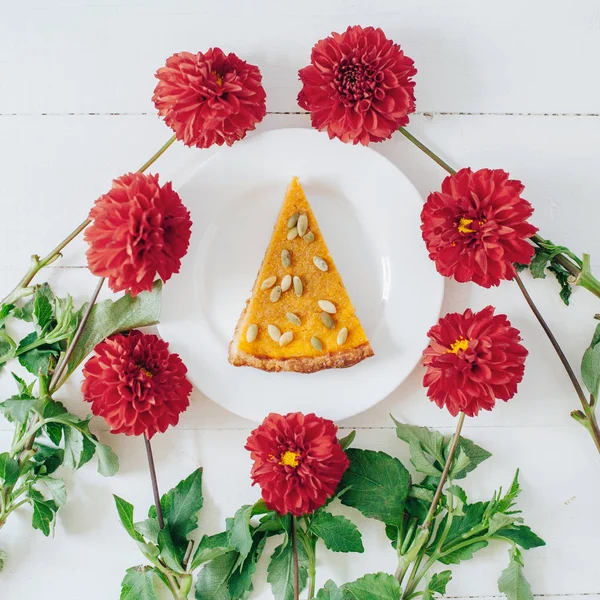 Sweet pumpkin pie on plate served on white table with red flowers