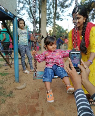 Bangalore, Karnataka / Hindistan-10 Aralık 2019: Güzel Hintli Çocuk, annesinin yardımıyla parkta sallanıyor.
