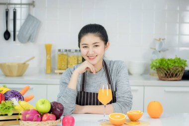 Bir bardak portakal suyuyla mutfak masasında oturan Asyalı genç kadın.