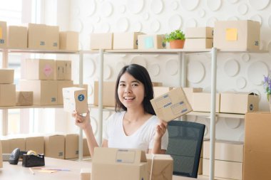 Mutlu genç bayan gülümsüyor, Güzel Asyalı kadın küçük bir işletmede başlıyor veya KOBİ ve kutunun üzerindeki listeyi işaretliyor. / çevrimiçi ticaret dünyası