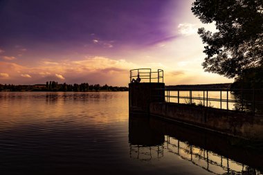 Genç adam gün batımında dinleniyor ve gölün kenarında oturuyor.