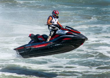 Huntington Beach, CA / USA - 7 Nisan 2019: Kaslı bir adam Pasifik Okyanusu 'nda son hızda jet ski ile yarışıyor, jet ski' de dururken okyanus dalgasından atlarken yer çekimine meydan okuyor. Adamın jet ski 'si siyah ve kırmızı, kaskı da öyle..