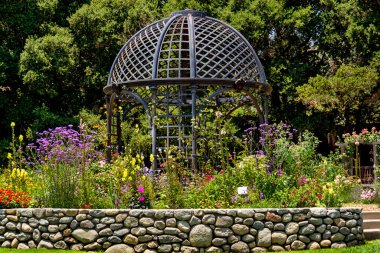Büyük, yıpranmış demir bir çardak güzel bahar çiçekleriyle çevrili bir bahçenin ortasında..