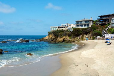 Laguna Beach, CA / USA - 09 / 02 / 2020: Pasifik Okyanusunda yüzen ve İşçi Bayramı 'ndan hemen önce kayalıklar ve lüks evlerle çevrili olan Wood' s Cove sahilinde güneşlenen insanlar.