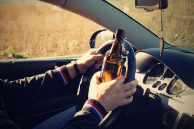 A drunken man driving a car with a bottle of alcohol in his hand.A man holds a driving wheel and a bottle of beer. clipart