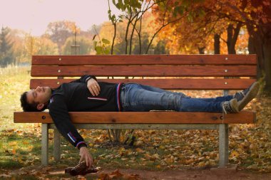 Gündüz vakti bankın altındaki çimenlerde uyuyan sarhoş bir genç adam. Elinde bir şişe alkol tutan ve bankın altında uyuyan genç bir adam. Gençler arasında alkolizm sorunu.