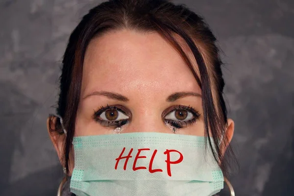 Tearful woman - medical worker - with blurry eyes and mask with inscription HELP.Tearful woman - medical worker - with blurry eyes and mask. Doctor or nurse helping patients with  treatment e.g. with covid-19.