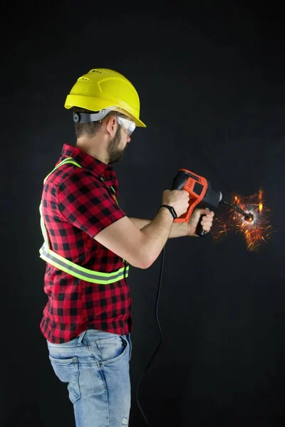 Construction Worker drills with a large demolition hammer  on black background. Construction worker with yellow crash helmet drills a hole in the wall. Sparks fly.