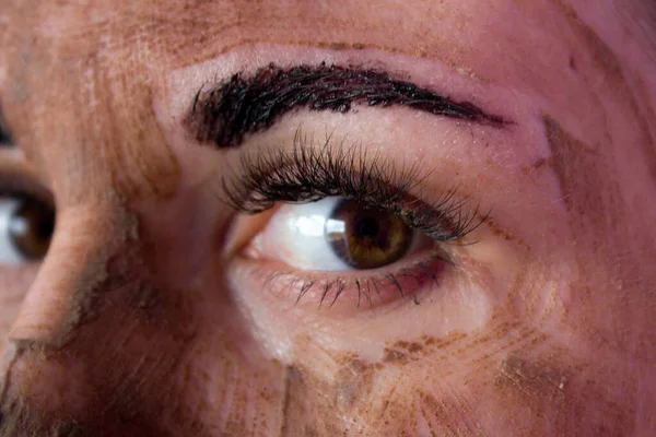 Beauty day. Close-up of a woman`s face. The woman has a clay face mask and eyebrows painted black.