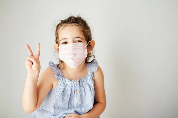 Menina feliz e com sinal de vitória com sua máscara protetora para evitar o contágio contra o vírus — Fotografia de Stock