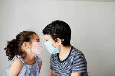 Koronavirüs zamanında maskeyle oynayan iki çocuk. Kardeşler Coronavirus yüzünden dışarı çıkmak için cerrahi maske takmaya çalışıyorlar. Salgını önlemek için sosyal mesafeli önlemler
