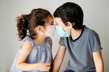 Koronavirüs zamanında maskeyle oynayan iki çocuk. Kardeşler Coronavirus yüzünden dışarı çıkmak için cerrahi maske takmaya çalışıyorlar. Salgını önlemek için sosyal mesafeli önlemler