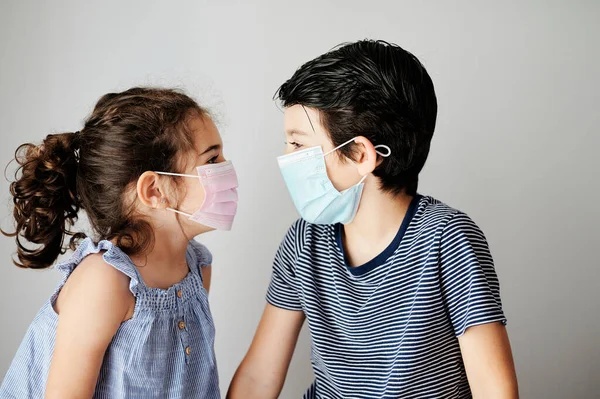 Koronavirüs zamanında maskeyle oynayan iki çocuk. Kardeşler Coronavirus yüzünden dışarı çıkmak için cerrahi maske takmaya çalışıyorlar. Salgını önlemek için sosyal mesafeli önlemler
