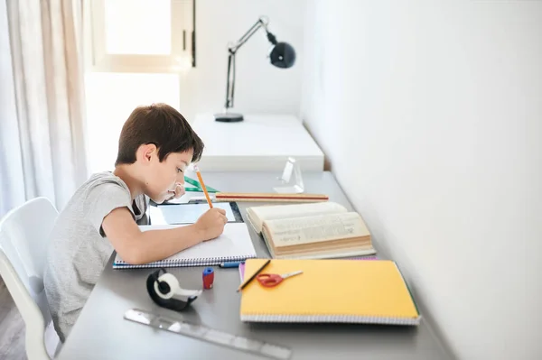Παιδί άγχος κάνει κατ 'οίκον δουλειά.Αγόρι στο τραπέζι μελέτη κάνει την εργασία με τη δράση άγχος.Τεμπέλης αγόρι κάνει την εργασία με το πρόσωπο τόνισε. — Φωτογραφία Αρχείου