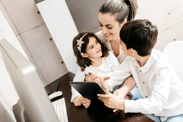 Çocuklarıyla orta yaşlı bir anne çalışma alanında dijital tablet kullanıyor.