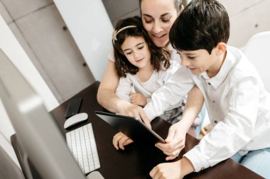 Çocuklarıyla orta yaşlı bir anne çalışma alanında dijital tablet kullanıyor.